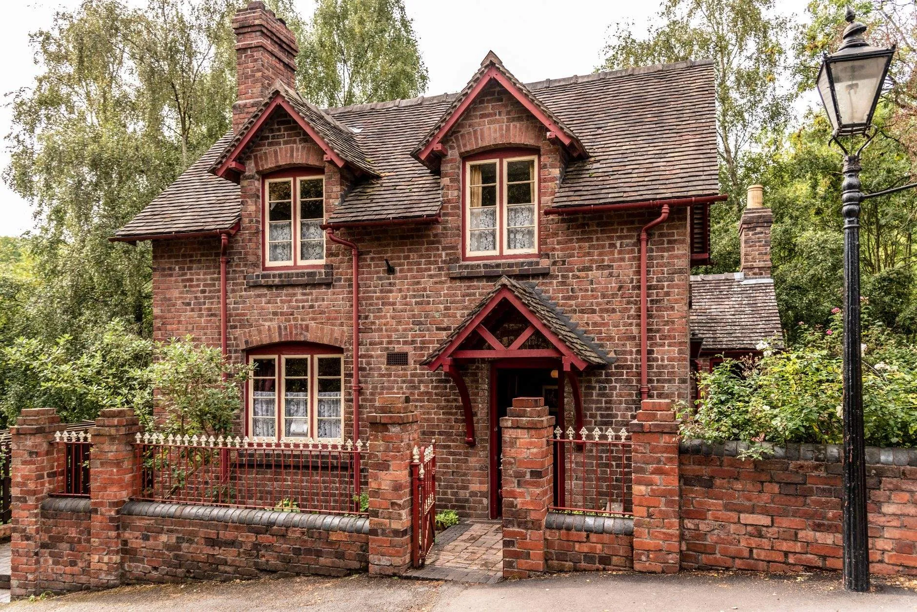 Red-brick Victorian lodge with two gabled dormers, a gabled porch and red railings