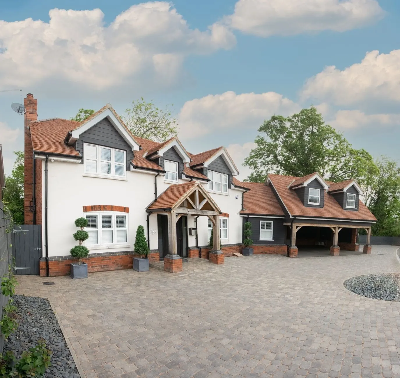 White-rendered detached house with grey weatherboarded dormers, a clay tile roof, an oak-framed porch and a double carport