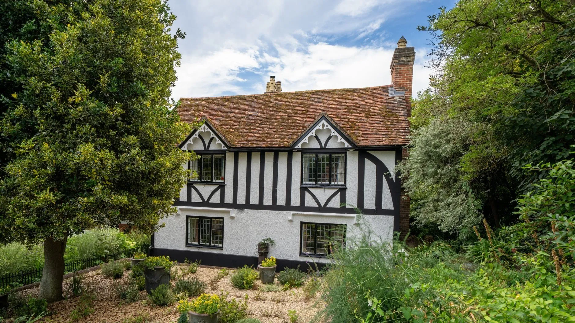 White rendered house with black timber framing and a clay tile roof behind a planted gravel garden